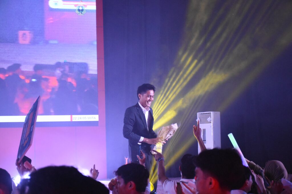 Pria berjas menerima bunga di atas panggung