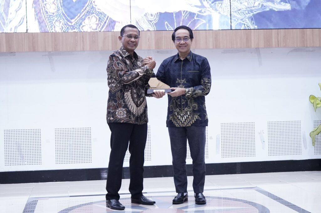 Dua pria berjabat tangan sambil memegang penghargaan