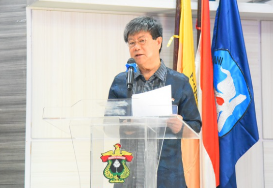 Man speaking at podium with flags behind