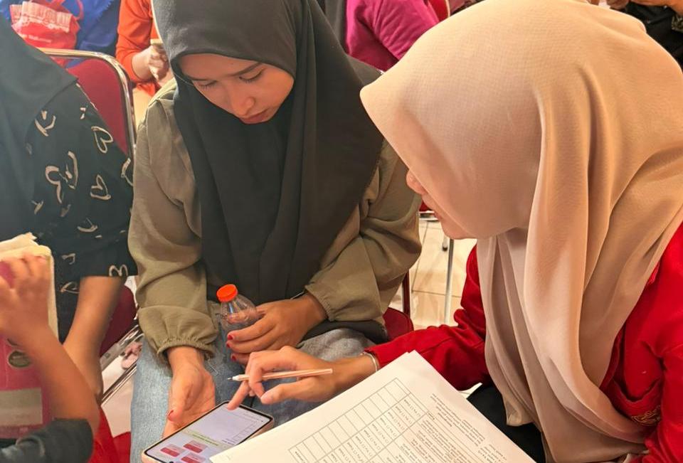 Dua wanita berhijab melihat ponsel dan formulir