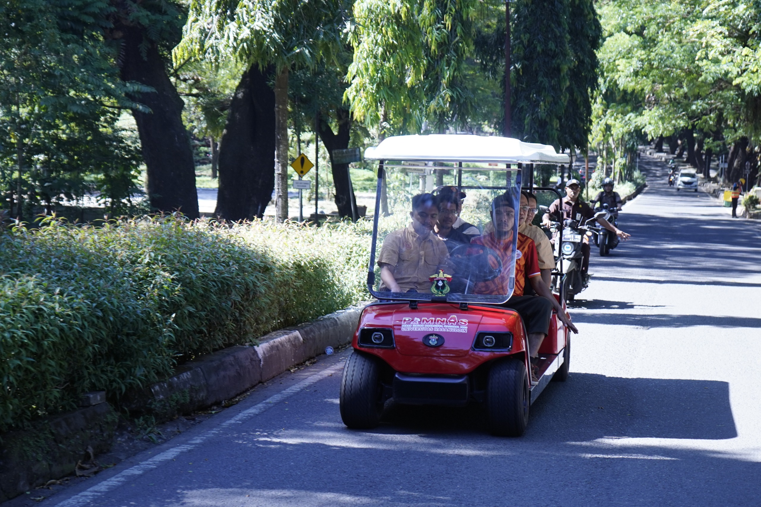 Mobil listrik kampus melaju di jalan rindang