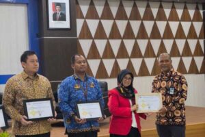 Empat orang menerima sertifikat penghargaan di ruangan resmi