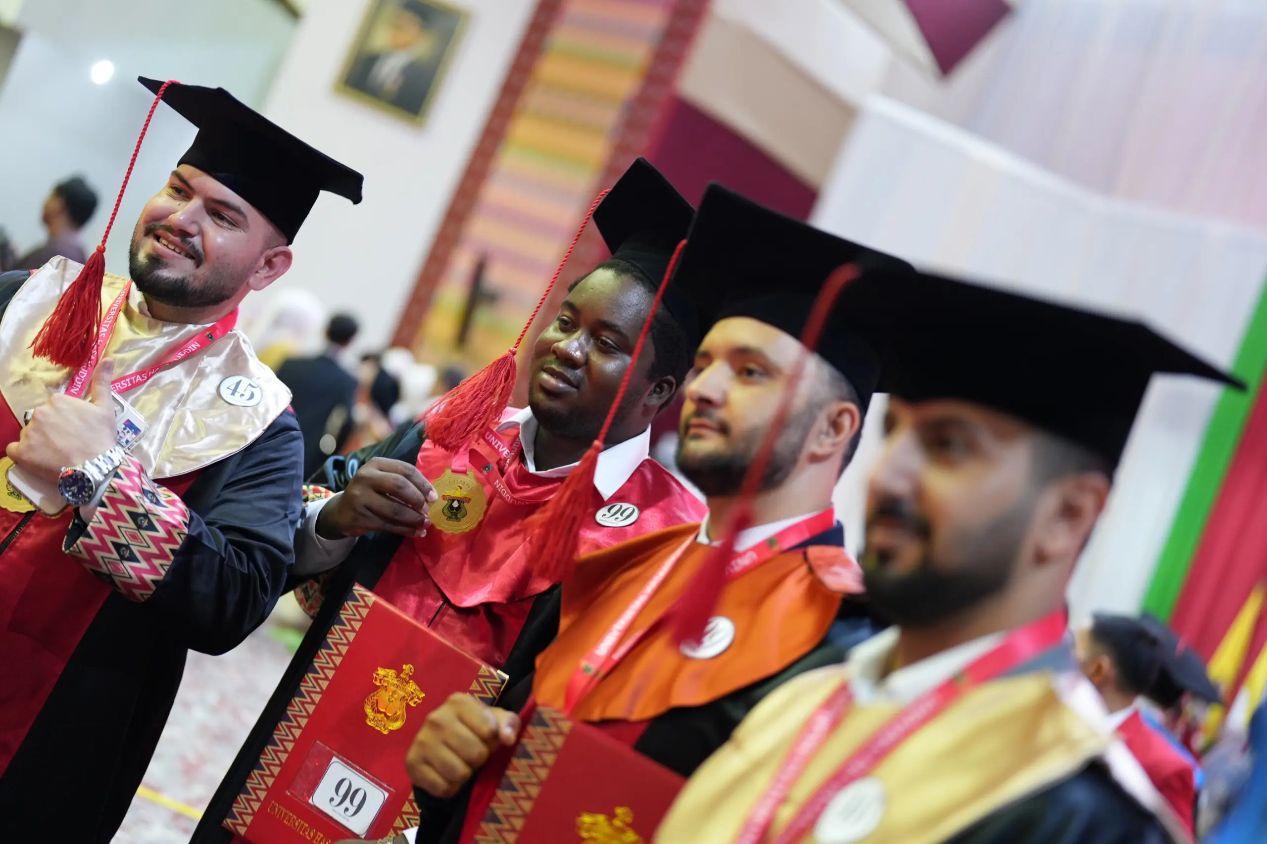 Graduates in caps and gowns holding diplomas indoors