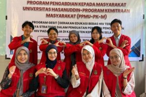 Mahasiswa berjaket merah berpose di depan banner