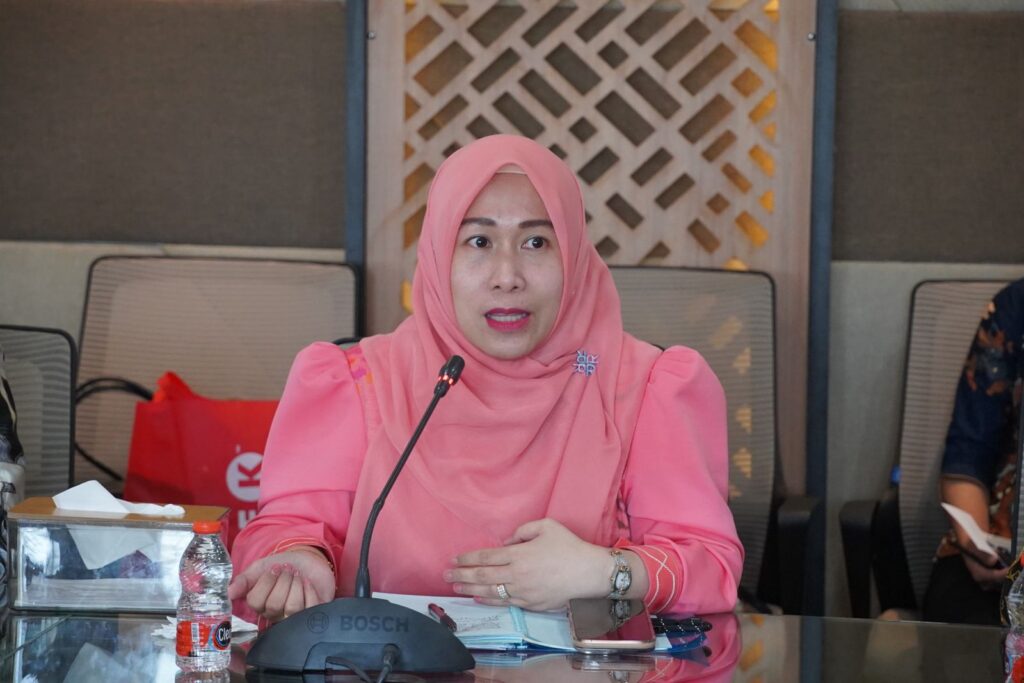 Perempuan berhijab pink berbicara di rapat resmi