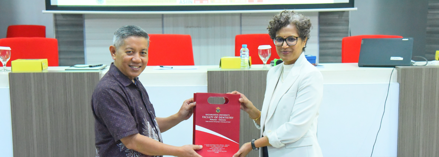 Two professionals exchanging university gift bag indoors
