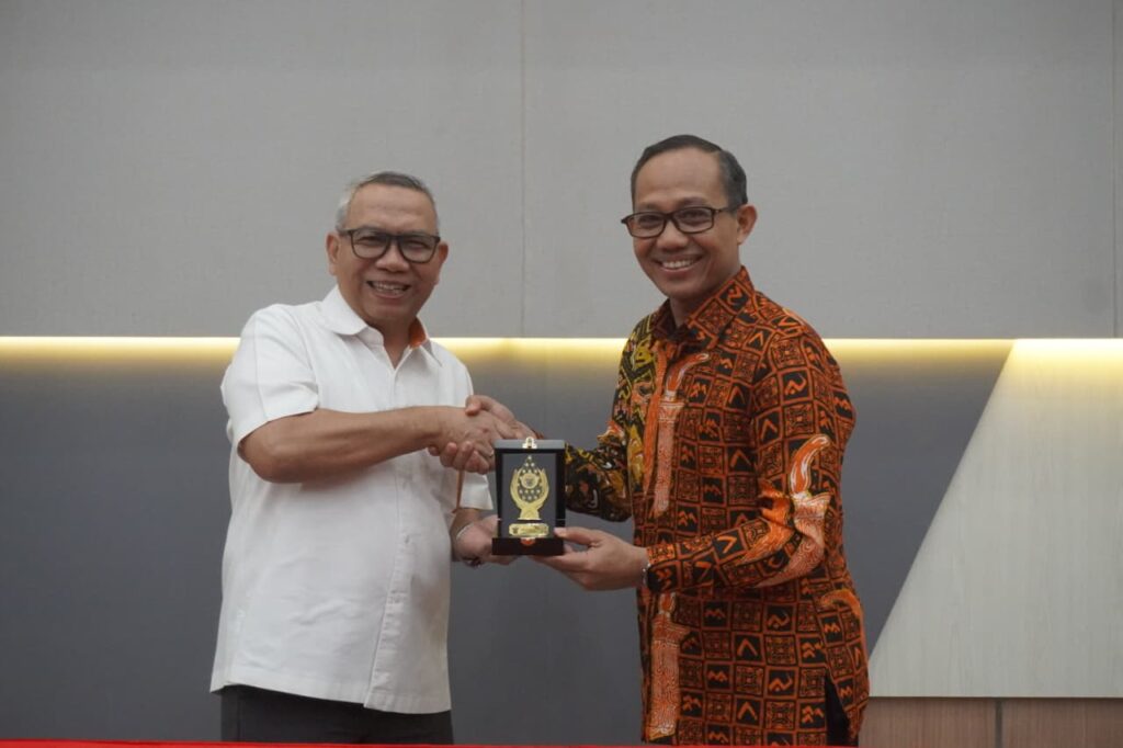 Dua pria berjabat tangan sambil memegang plakat penghargaan