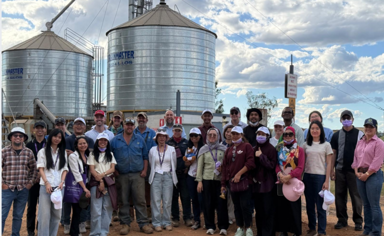 Group posing in front of large farm silos