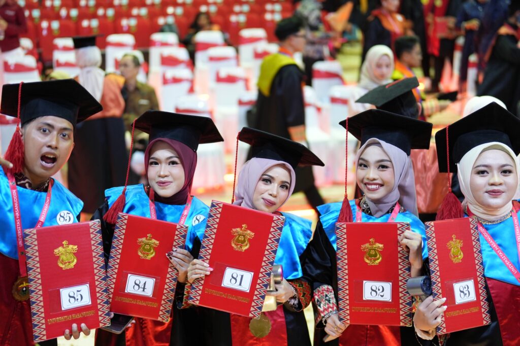 Graduates holding diplomas at indoor commencement ceremony