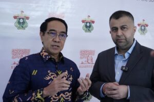 Dua pria berdiskusi di depan backdrop universitas