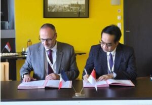 Dua pejabat menandatangani dokumen dengan bendera Indonesia Prancis