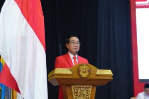 Pria berjas merah berpidato di podium dekat bendera Indonesia