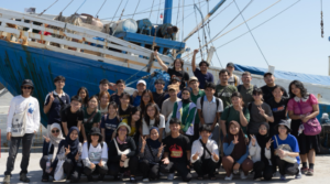 Large group posing in front of blue fishing boat