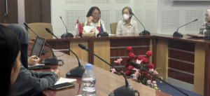 Women seated at conference table with microphones and flags