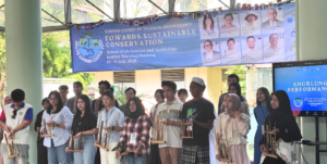 Students holding angklung instruments under event banner
