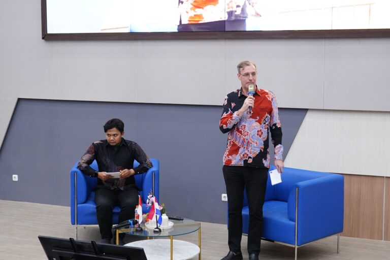 Pria berbicara di acara panel dengan bendera Indonesia