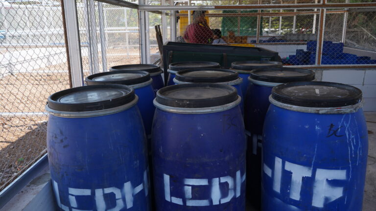 Blue lidded barrels stored behind chain-link fencing