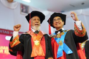 Dua akademisi bersorban wisuda mengangkat tangan penuh semangat