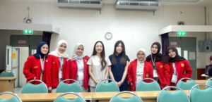 Eight women pose in a classroom behind empty chairs