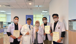 Five masked healthcare workers display certificates in a hospital hallway.
