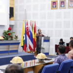 Speaker addresses audience beside international flags in conference hall