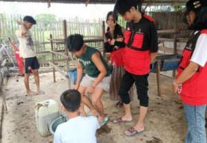 Youth group gathers around container in rustic animal shelter