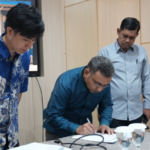 Three men review documents as one signs paperwork.