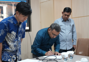 Three men review documents as one signs paperwork.