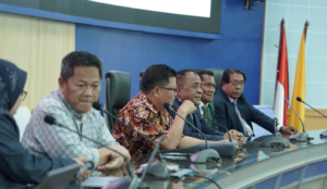 Officials seated at conference table with microphones and flags