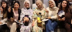 Six women seated together at an indoor event