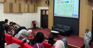 Presenter addresses audience beside projected sustainability-themed slide