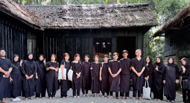 Group in black outfits standing before traditional wooden house