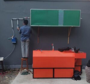 Worker installs piping beside outdoor orange workstation