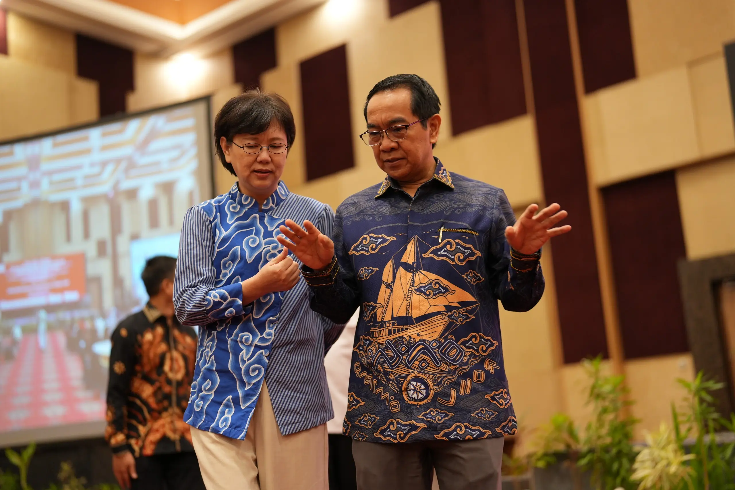 Dua peserta berdiskusi dalam acara formal mengenakan batik biru.