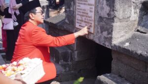 Pria berjas merah menunjuk prasasti situs bersejarah