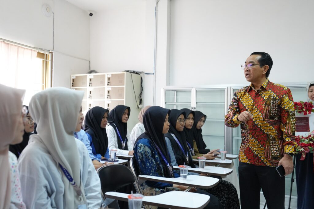 Pria berbaju batik berbicara kepada mahasiswi di kelas