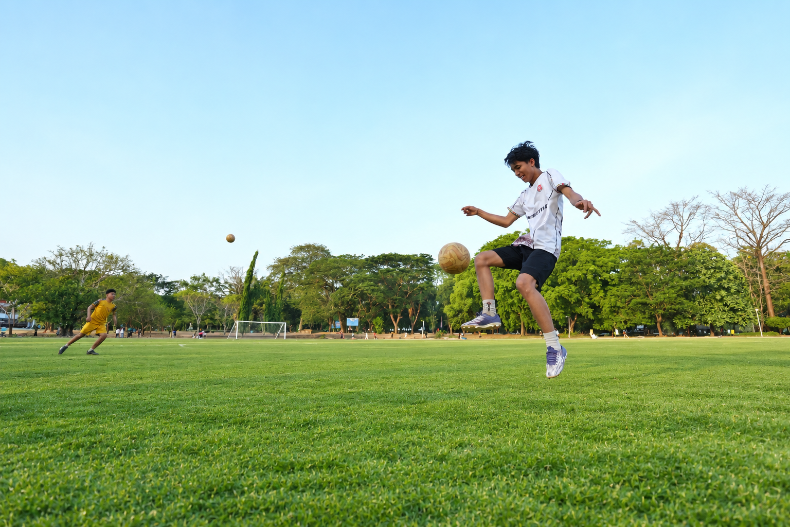 Remaja menendang bola di lapangan sepak bola hijau