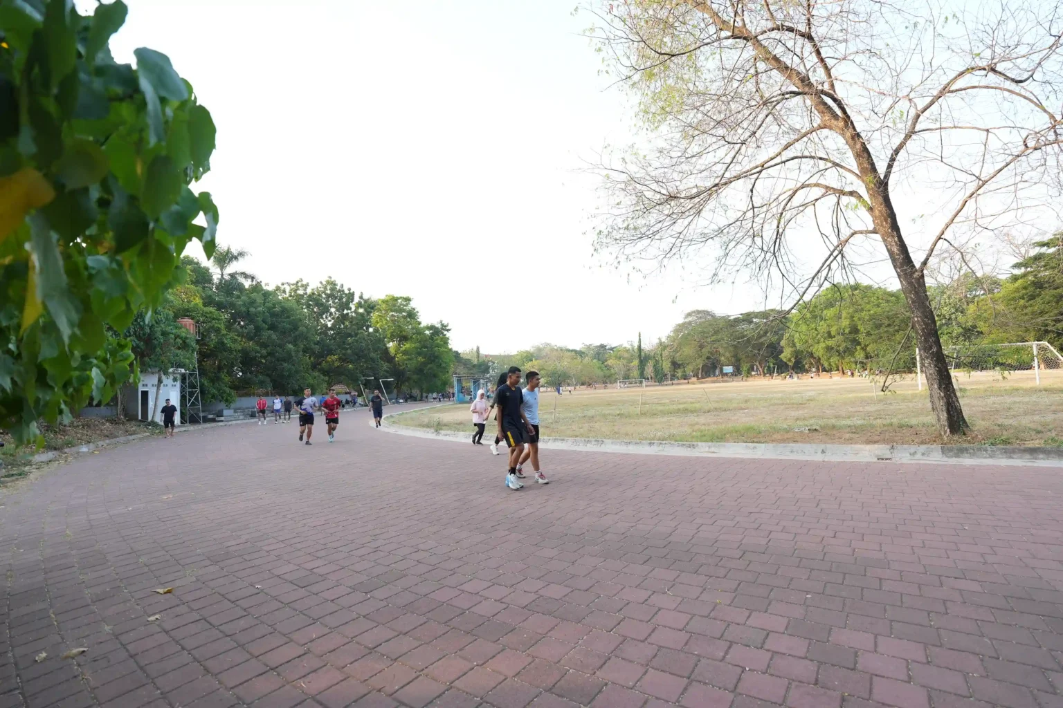 Orang berolahraga di jalur taman dekat lapangan sepak bola